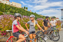 Gut gelaunte Radfahrer halten an, um gemeinsam ihr nächstes Ziel zu planen, während im Hintergrund die Veste Oberhaus emporragt.