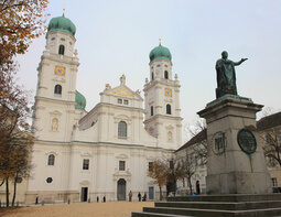 Eine Bronzeskulptur steht auf dem Domplatz vor dem kirchlichen Wahrzeichen, dem Stephansdom in Passau.