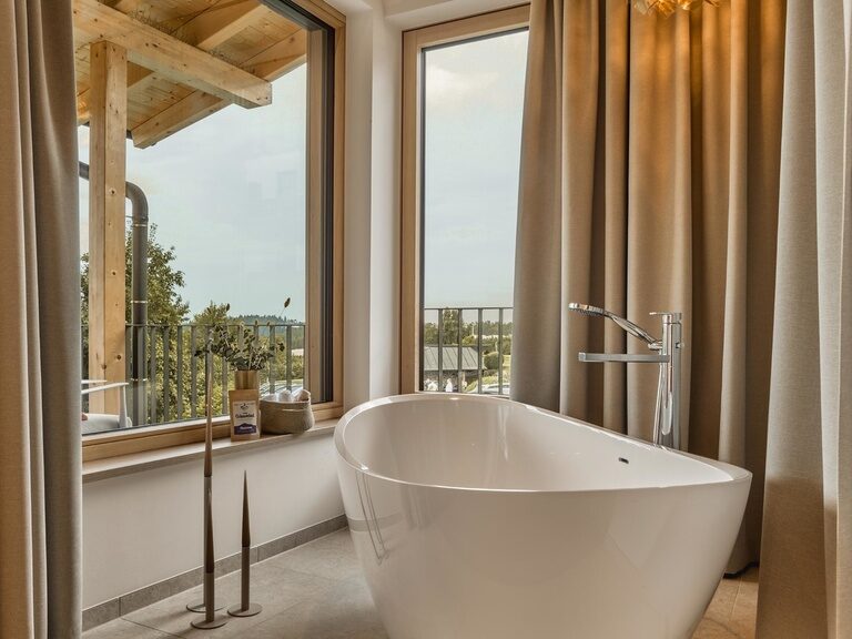 Modernes Badezimmer in einer Spa-Loft des Hotel Anetseder mit freistehender Badewanne und Ausblick durch große Fenster.