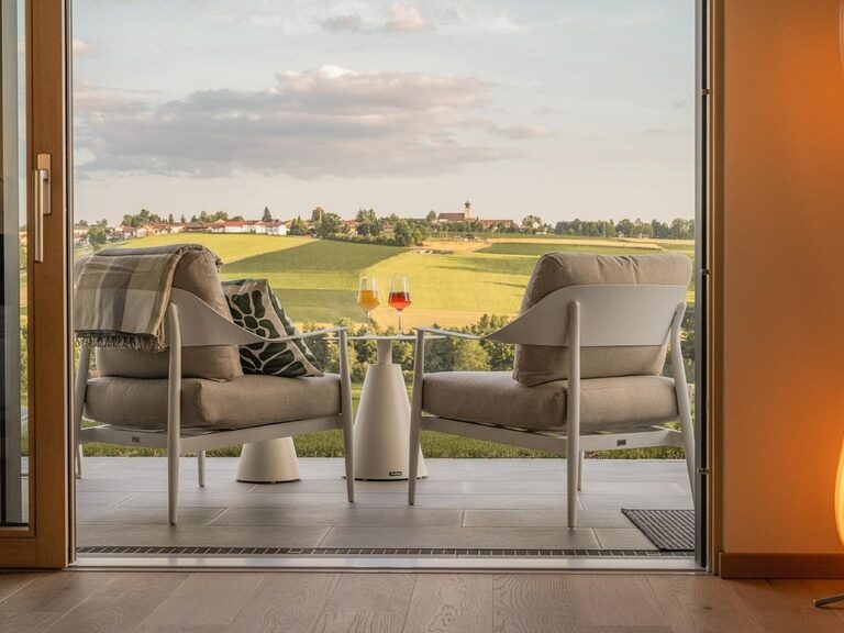 Auf der Terrasse der Spa Lofts des Landhotels Anetseder stehen zwei gefüllte Weingläser bereit, während sich vor ihnen eine atemberaubende Landschaft entfaltet.